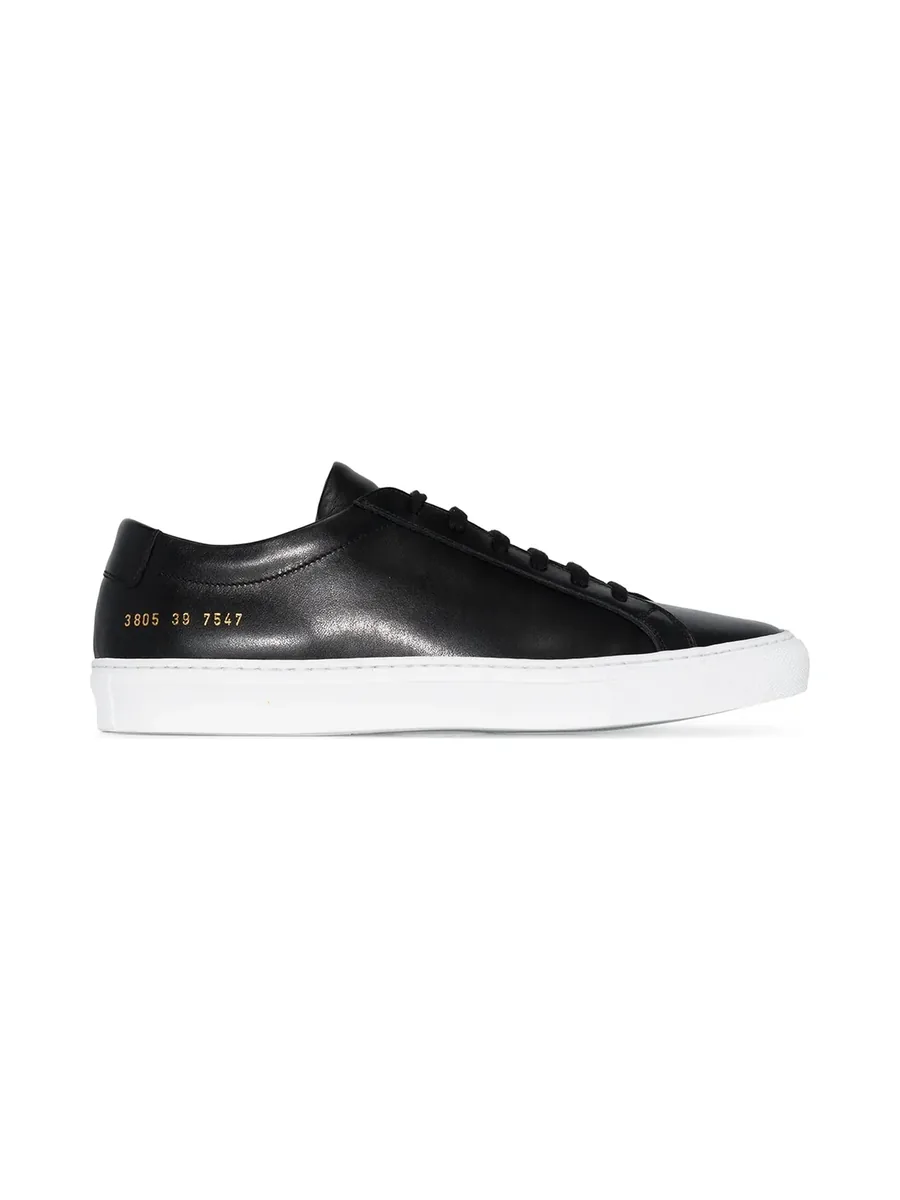 Black leather low-top sneaker with white sole and gold serial number, side view