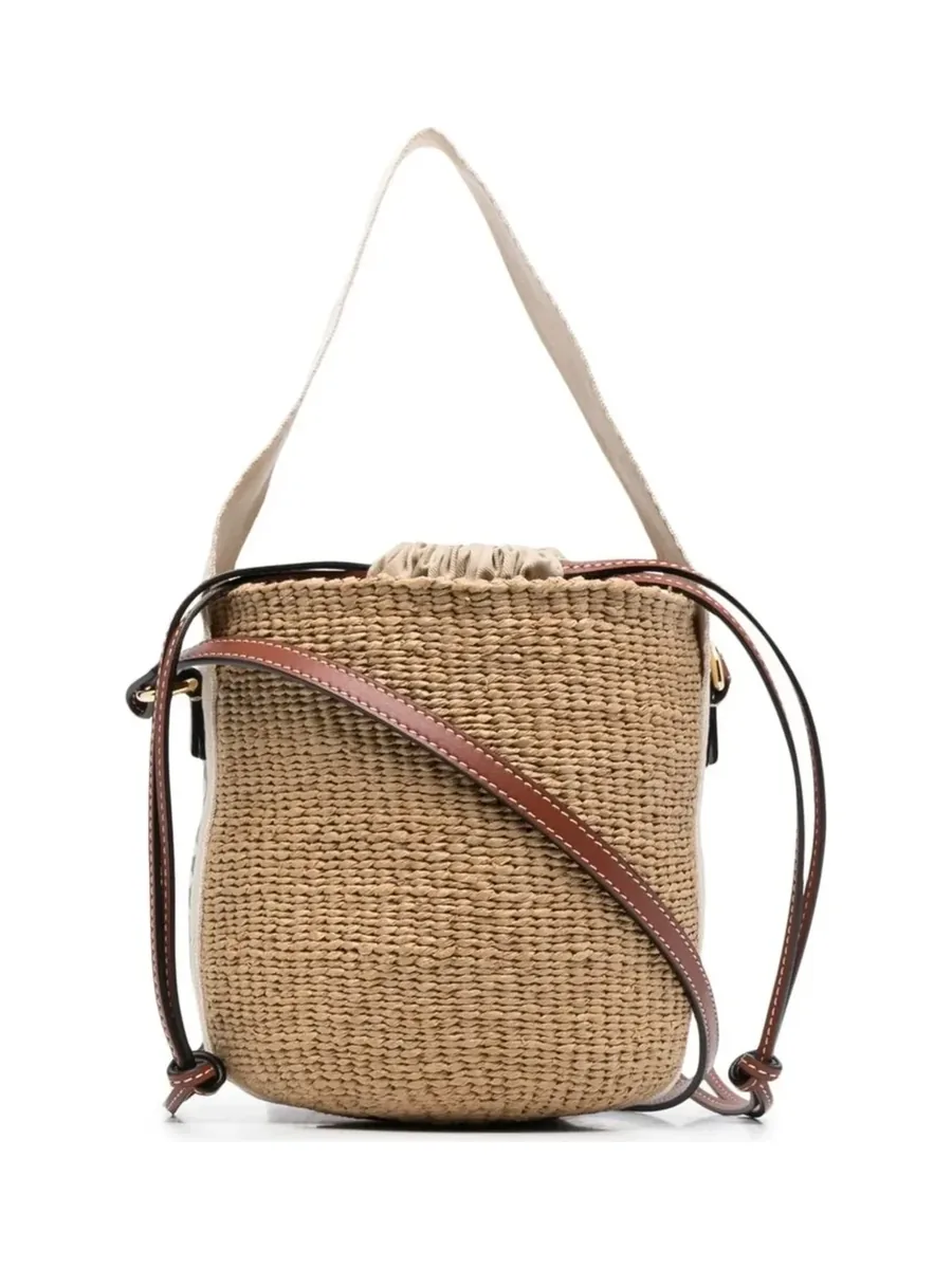 Small woven basket bucket bag with a drawstring top, brown leather cords and a cream handle, front view