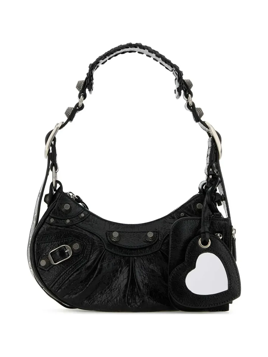 Black studded leather shoulder bag with a buckle, heart mirror charm and curved strap, front view
