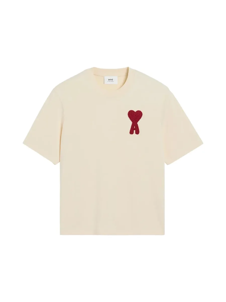 Beige crew-neck T-shirt with a red heart logo patch at the chest, front view